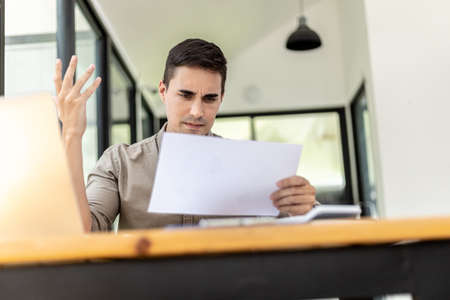 A businessman holding a sales document that the sales department summarizes, he looks displeased when he sees reports of falling sales, he shows signs of stress. Failed sales management concept.の写真素材
