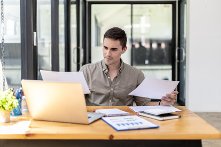 A businessman holding a sales document that the sales department summarizes, he looks displeased when he sees reports of falling sales, he shows signs of stress. Failed sales management concept.の写真素材