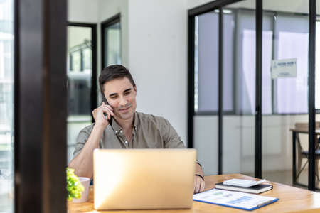 Man talking on the phone in the office, He is a businessman executive of a startup company founded with partners, He is a young and energetic executive and the company's earnings continue to grow.の写真素材