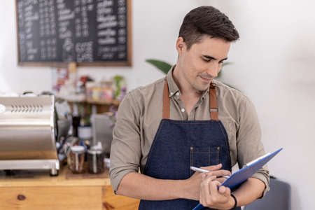 Handsome man holding blue folders in a cafe, he is preparing to open a shop to serve customers, a male employee opens a shop to serve food and drinks. Food and beverage service concept.の写真素材