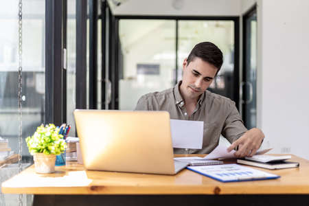 Young businessman sitting in the office at his company, he is checking the correctness of company financial documents, young businessman running a startup business is constantly profitable.の写真素材