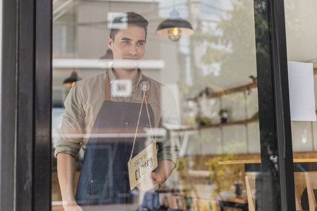 Handsome man holding a sign in front of a shop, a cafÃ© employee standing holding a sign saying open-close, he's flipping a sign saying "closed". Cafe food and beverage service concept.の写真素材