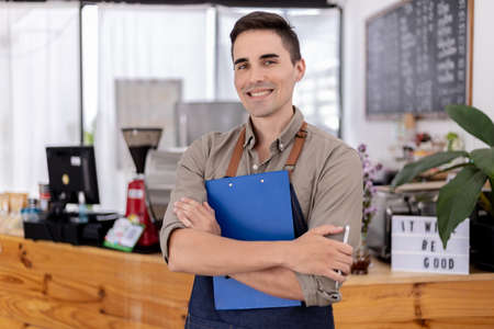 A handsome man standing in a cafe, he is a cafe worker, he is preparing to open a shop to serve customers, a male employee opens a shop to serve food and drinks. Food and beverage service concept.の写真素材