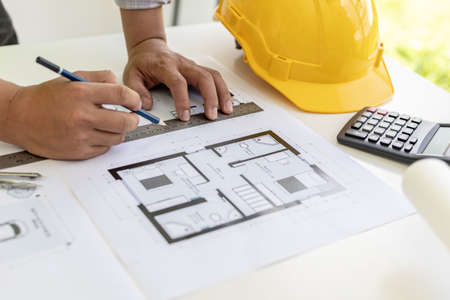 Architect engineer using a pencil to write on the blueprints he has designed, he is checking and revising the drawings before sending the work to the customers. Design and interior design ideas.の写真素材