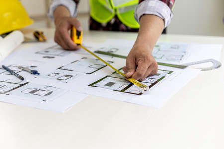 The male architect uses a tape measure to measure the house designs, he is checking the house plans...