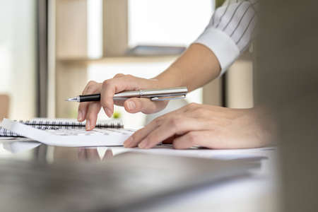 financial business woman pressing a white calculator, she uses a calculator to calculate the numbers in the company's financial documents that employees in the department create as meeting documents.の写真素材