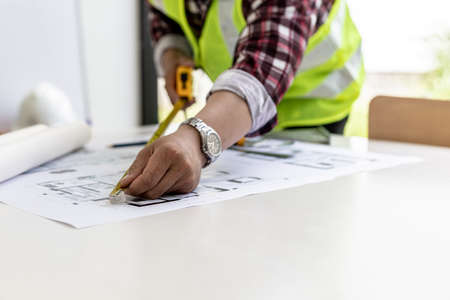 The male architect uses a tape measure to measure the house designs, he is checking the house plans that he has designed before sending it to the customers, he designs the house and the interior.の写真素材