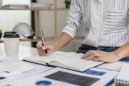Business woman is taking notes in a notebook, she is checking sales documents and financial documents in her private office, she is the executive of a startup company. Business administration concept.の写真素材
