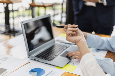 A female employee holding a pen and pointing at a laptop screen, she is attending a meeting with the management team to finalize the company's financial reports. Startup company meeting concept.の写真素材