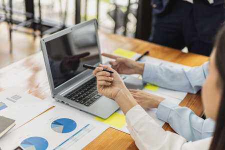 A female employee holding a pen and pointing at a laptop screen, she is attending a meeting with the management team to finalize the company's financial reports. Startup company meeting concept.の写真素材