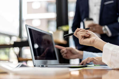 A female employee holding a pen and pointing at a laptop screen, she is attending a meeting with the management team to finalize the company's financial reports. Startup company meeting concept.の写真素材