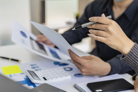 Meeting room of a startup company where two businessmen are looking at financial information from documents, they are meeting on monthly finance topics. Concept of financial management.の写真素材