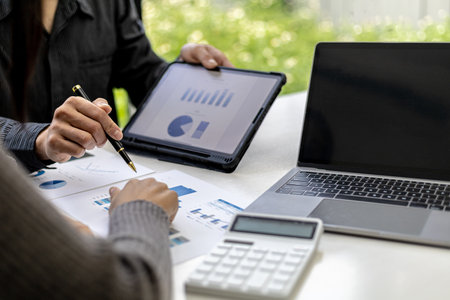 Close-up photo of two businessmen pointing at a sales data sheet in graph format, they are meeting...