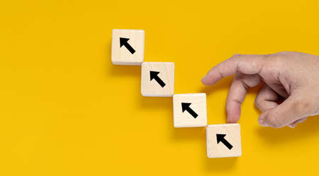 A square wooden block is placed on a yellow background, on the wooden block showing an up arrow and...