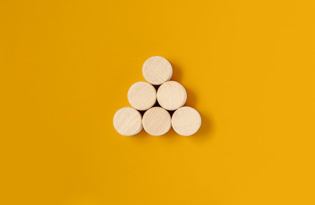 The circular wooden blocks are placed on a yellow background, the wooden blocks are arranged in a triangular shape. Wood block concept, banner with copy space for text, poster, mockup template.の写真素材