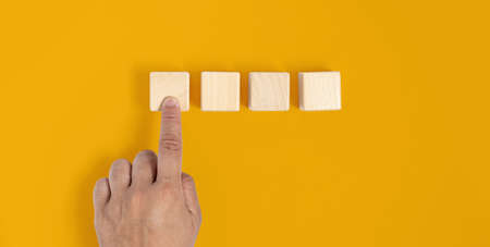 Square wooden block is placed on a yellow background, hand pressed to the first wooden block similar to pressing a button. Wood block concept, banner with copy space for text, poster, mockup template.の写真素材