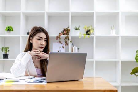 Beautiful Asian young woman looking at information on a laptop, concept image of Asian business woman working smart, modern female executive, startup business woman, business leader woman.の写真素材