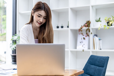 A beautiful Asian businesswoman standing in a room, she is talking business with her partner through a laptop messenger, she is a female executive of a startup company. Concept of financial managementの写真素材