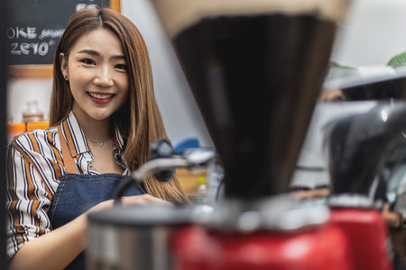 Portrait of a beautiful Asian woman in an apron using a coffee machine, she owns a coffee shop, concept of a food and beverage business. Store management by a business woman.の写真素材