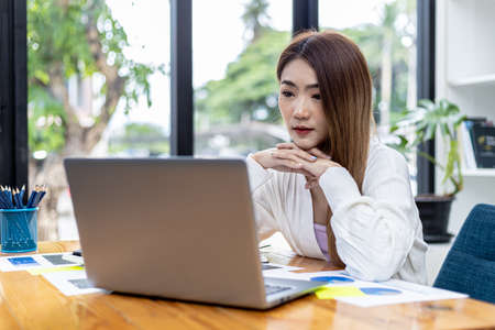 Beautiful Asian young woman looking at information on a laptop, concept image of Asian business woman working smart, modern female executive, startup business woman, business leader woman.の写真素材