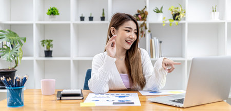 Beautiful Asian businesswoman sitting in her private office, she is talking to her partner via video call on her laptop, she is a female executive of a startup company. Concept of financial managementの写真素材