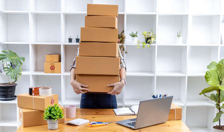 Beautiful Asian woman lifting a bunch of parcels, she owns an online store, she packs and ships...
