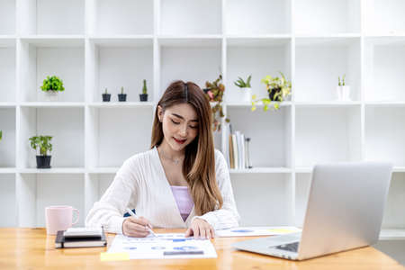 A beautiful Asian businesswoman sitting in her private office, she is checking company financial documents, she is a female executive of a startup company. Concept of financial management.の写真素材