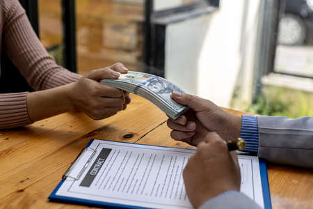 Picture of two people handing over a dollar, they are business partners who are doing corrupt behavior by bribing them for illegal mutual benefit. The concept of business fraud and bribery.の写真素材