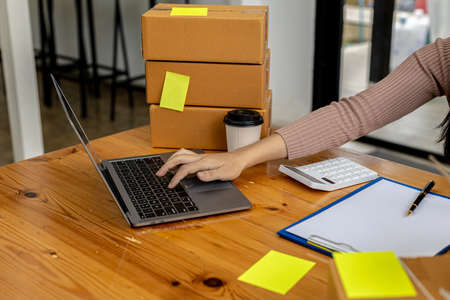 Woman who runs an e-commerce business check a list of customers on her laptop before shipping to...
