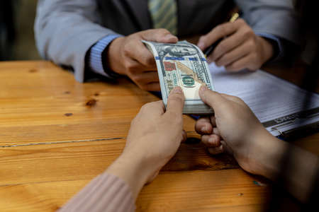 Picture of two people handing over a dollar, they are business partners who are doing corrupt behavior by bribing them for illegal mutual benefit. The concept of business fraud and bribery.の写真素材