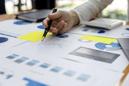 Close-up businessman holding a pen and pointing at a bar chart on a company financial document, he is analyzing historical financial data to plan how to grow the company. Financial concept.の写真素材