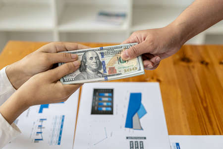 Picture of two people handing over a dollar, they are business partners who are doing corrupt behavior by bribing them for illegal mutual benefit. The concept of business fraud and bribery.の写真素材