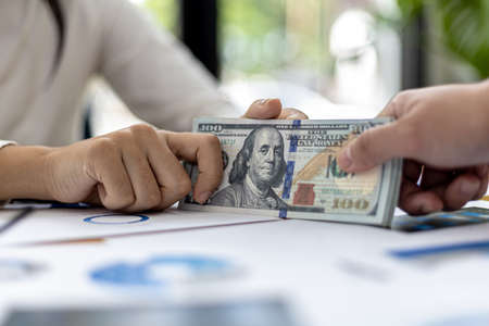 Picture of two people handing over a dollar, they are business partners who are doing corrupt behavior by bribing them for illegal mutual benefit. The concept of business fraud and bribery.の写真素材