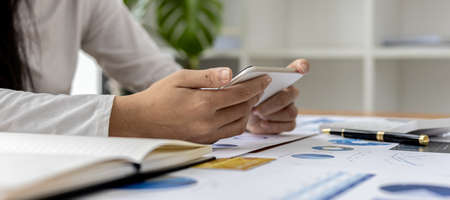businesswoman holding a mobile phone, she is looking at information on mobile phone that the financial officer sends through an online messaging program. Financial concepts.の写真素材