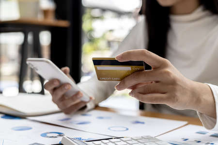 A woman holding a smartphone and a credit card, she is doing online shopping through a smartphone app by paying credit card payments. Online shopping ideas with a credit card.の写真素材