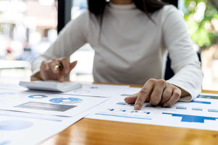 A financial scholar is pointing at a document with a pen, she is analyzing and checking company...