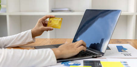 A woman typing on a laptop keyboard, she is filling out her credit card information to pay for an...