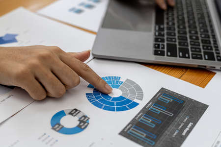 A businesswoman is checking company financial documents and using a laptop to talk to the chief...