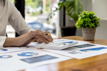 Close-up of a businesswoman using a white calculator, a financial businessman examining the numerical data on a company financial document, she uses a calculator to verify the accuracy of numbers.の写真素材