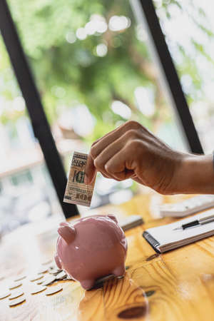 Businessman holds dollar bills in a piggy bank. Placing coins in a row from low to high is comparable to saving money to grow more. The concept of growing savings and saving by investing in stock fundの写真素材