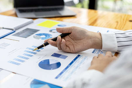 Close-up businesswoman's hand holding a pen pointing at a bar chart on a corporate financial...