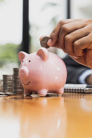 A businessman holding a coin in a piggy bank. Placing coins in a row from low to high is comparable to saving money to grow more. The concept of growing savings and saving by investing in stock funds.の写真素材