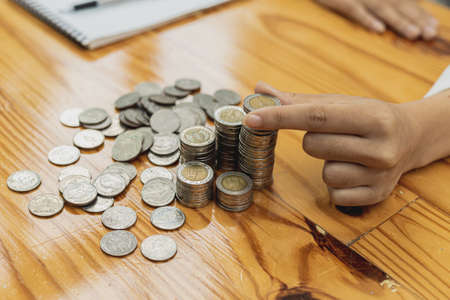 Businesswoman putting a coin on a pile of coins. Placing coins in a row from low to high is...
