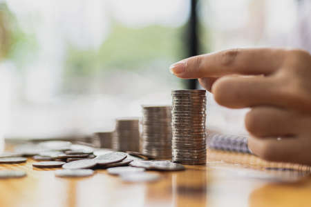 Businesswoman putting a coin on a pile of coins. Placing coins in a row from low to high is...