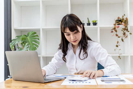 A beautiful Asian businesswoman sitting in her private office, she is checking company financial documents, she is a female executive of a startup company. Concept of financial management.の写真素材