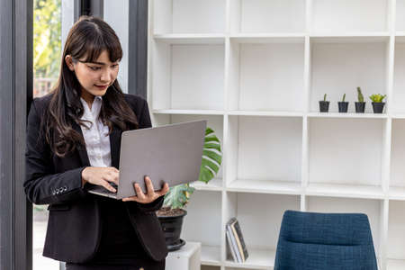 A beautiful Asian businesswoman in her private office, she is checking company financial documents,...