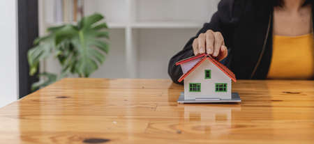 Woman puts her hand on top of a miniature house model, photo of home insurance concept, when buying a new home should have home insurance to be sure if there is any danger to the home.の写真素材