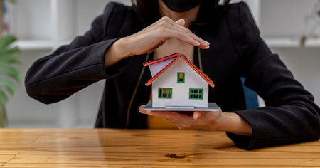 Woman puts her hand on top of a miniature house model, photo of home insurance concept, when buying a new home should have home insurance to be sure if there is any danger to the home.の写真素材