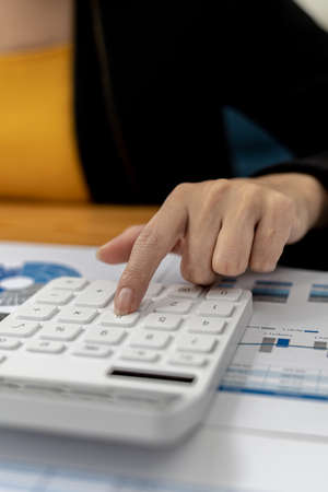 Close-up of a businesswoman using a white calculator, a financial businessman examining the numerical data on a company financial document, she uses a calculator to verify the accuracy of numbers.の写真素材
