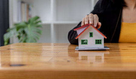 Woman puts her hand on top of a miniature house model, photo of home insurance concept, when buying a new home should have home insurance to be sure if there is any danger to the home.の写真素材